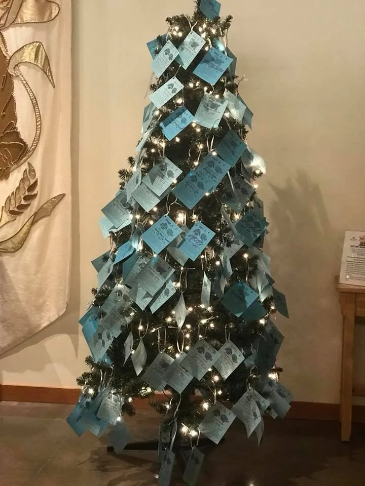 Giving tree covered with blue paper tags listing gift wishes from local children.